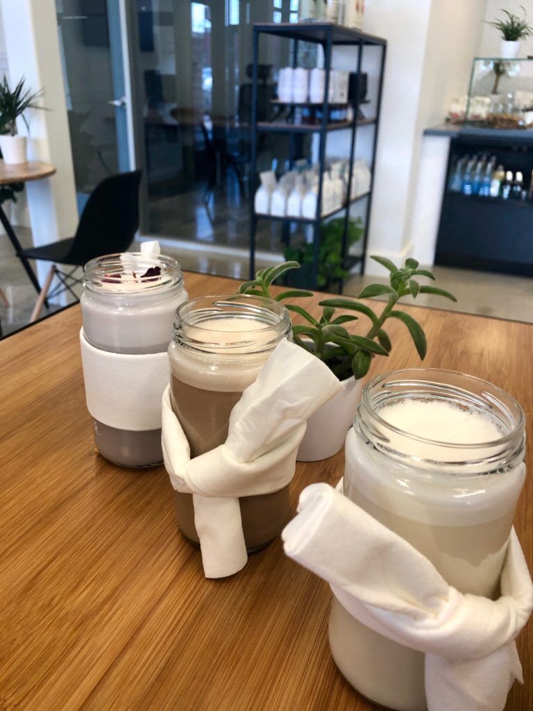 Blüm Specialty Coffee and tea Emerald Green,Moroccan Mint and Raspberry Rose tea lattes in glass jars tied with a white napkin on a table the coffee shop