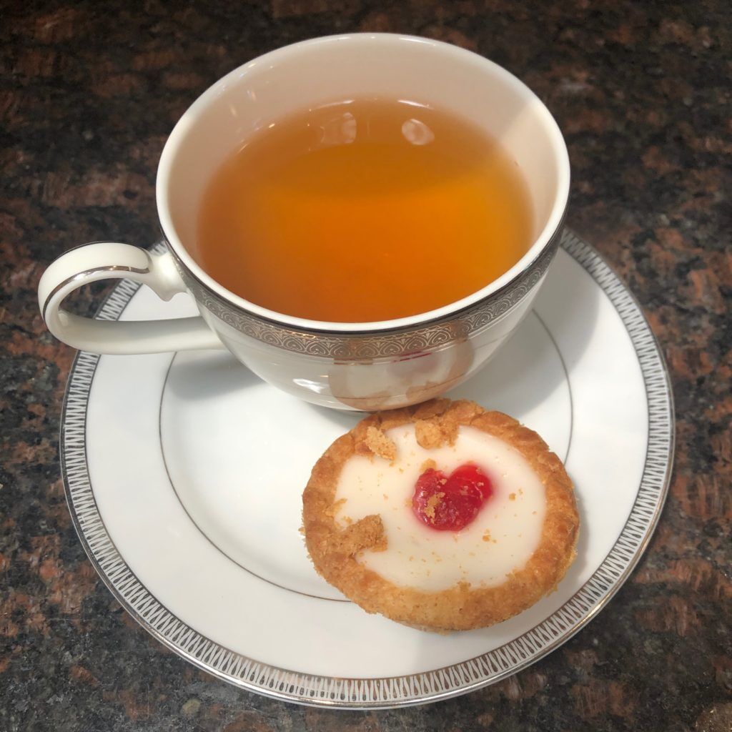 Cherry Bakewell tea in a white teacup and a Mr Kiplings Cherry Bakewell dessert on the tea saucer with the tea.