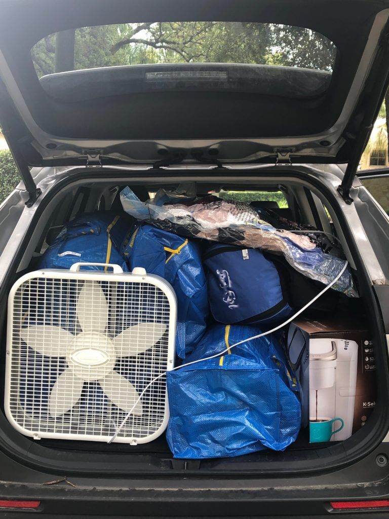 Trunk of an SUV packed full with college items:Ikea bags, fan, vacuum sealed bags, back pack.
